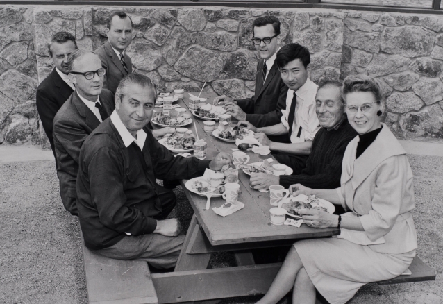 Nick Webster sits at a picnic table with New York Philharmonic musicians and Assistant Conductor Seiji Ozawa.