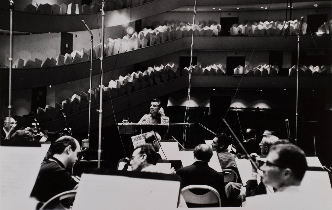 Black-and-white photo of the orchestra playing to a concert hall with large pieces of foam in the seats.