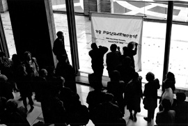Black and white photo of people gathered holding an AIDS memorial quilt panel.